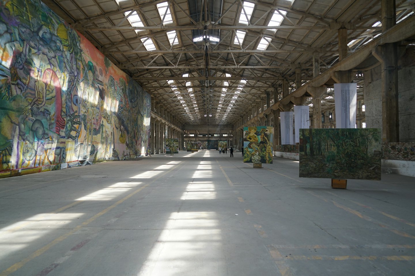 Persone passeggiano in una spaziosa galleria d'arte industriale con murales colorati.
