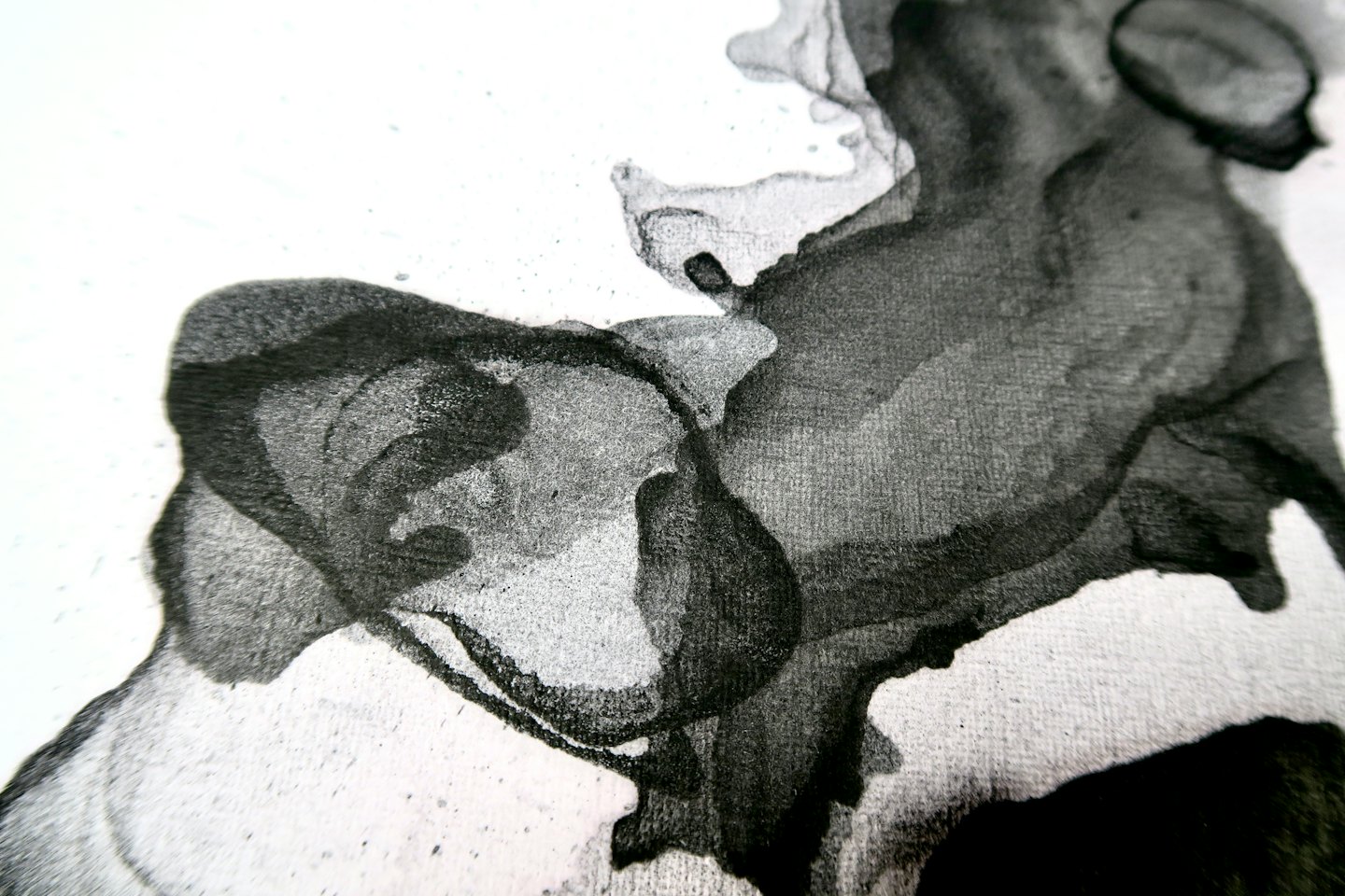 Macchie di inchiostro nero si diffondono su carta bianca in forme organiche astratte.